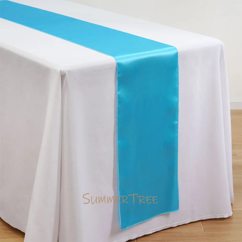 Elegant satin table runner in light blue and white on a draped white tablecloth.