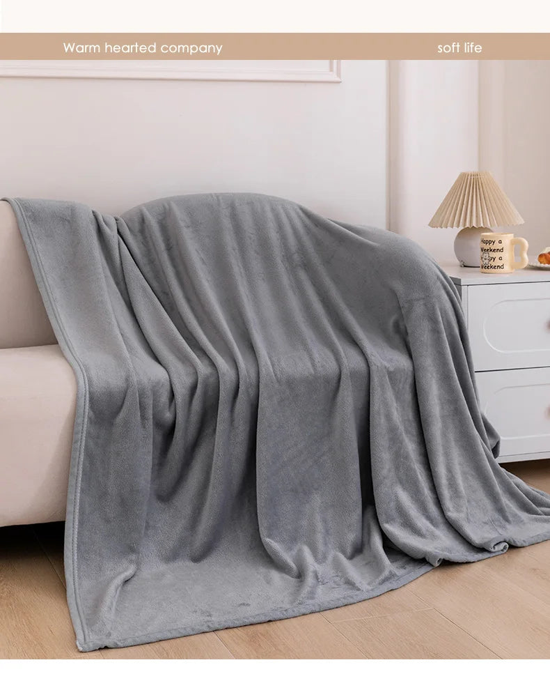 A soft gray flannel throw blanket draped on a sofa, with a white lamp and decorative items in the background.