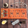 Orange tarot card storage pouch with decorative elements and natural stones and pine cones