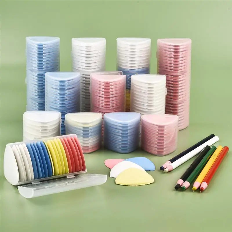 A collection of colorful erasable fabric chalk markers in various shades of blue, pink, and white are displayed on a green su