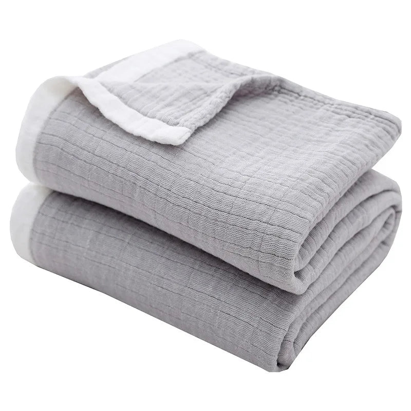 Gray muslin throw blanket folded and rolled with white trim