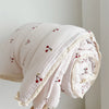 A rolled pink muslin blanket with a small red floral print is shown against a light background.