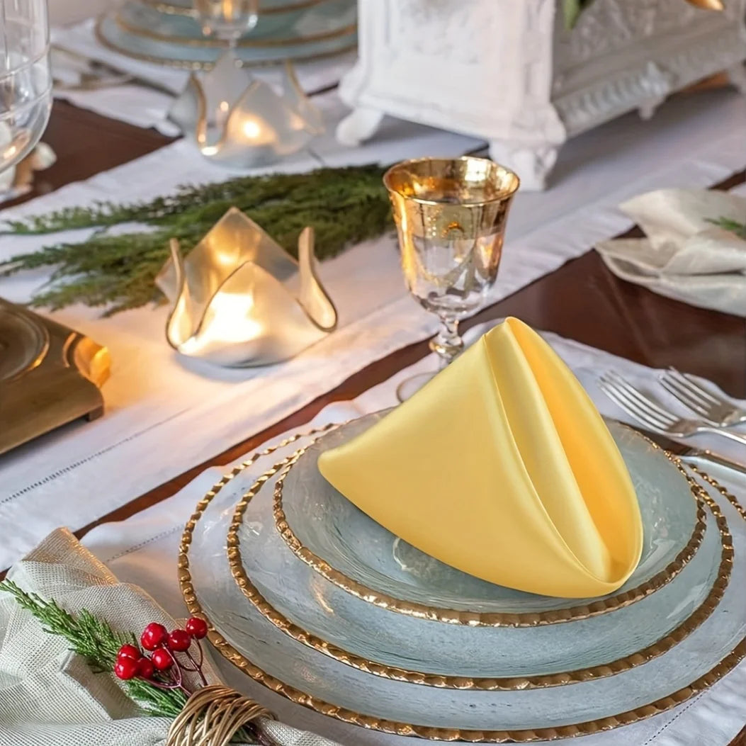 A stack of yellow silky satin dinner napkins on a tiered plate set for a formal table setting.