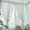 White French country lace curtains with beaded phoenix tail designs hanging in a bright window.