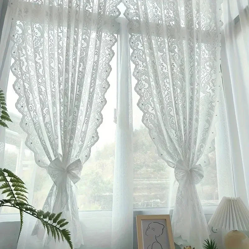 White French country lace curtain with beaded phoenix tail design hanging in a window.