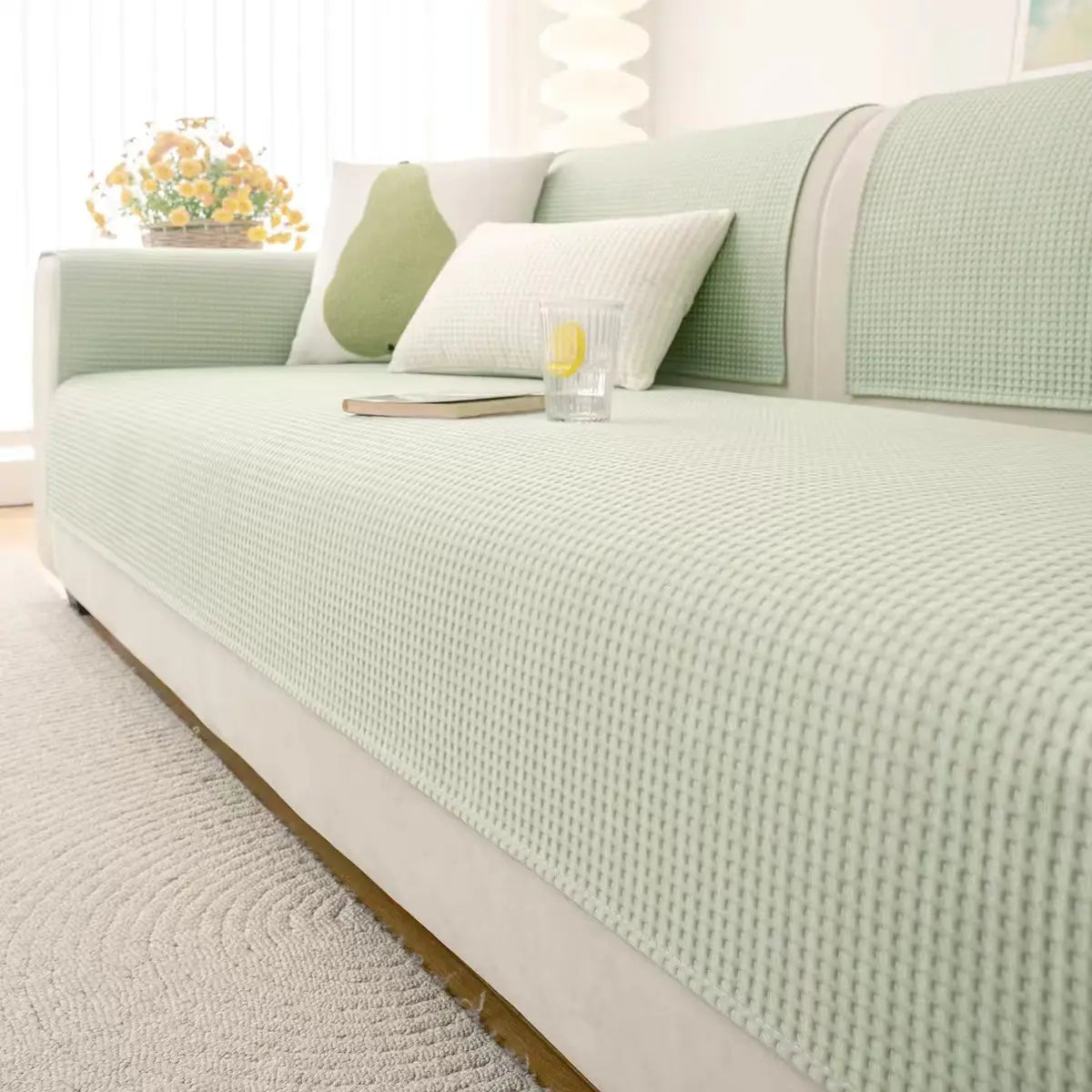 A light green machine washable anti-slip sofa slipcover with white pillows and a neutral rug.