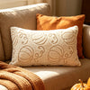 A beige sofa features a white fuzzy maple leaf throw pillow and an orange accent pillow, with a golden pumpkin visible.