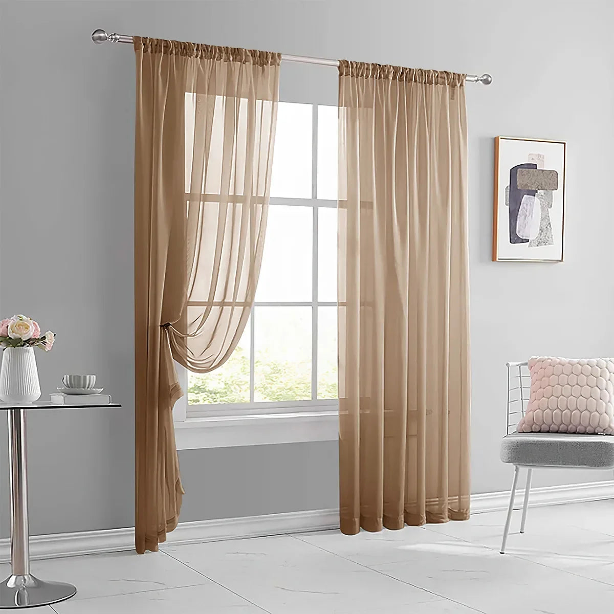 A pair of beige sheer curtains hanging in a window frame in a modern living room setting.