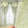 Light green sheer window curtains with white lace trim and floral embroidery shown hanging in a window.