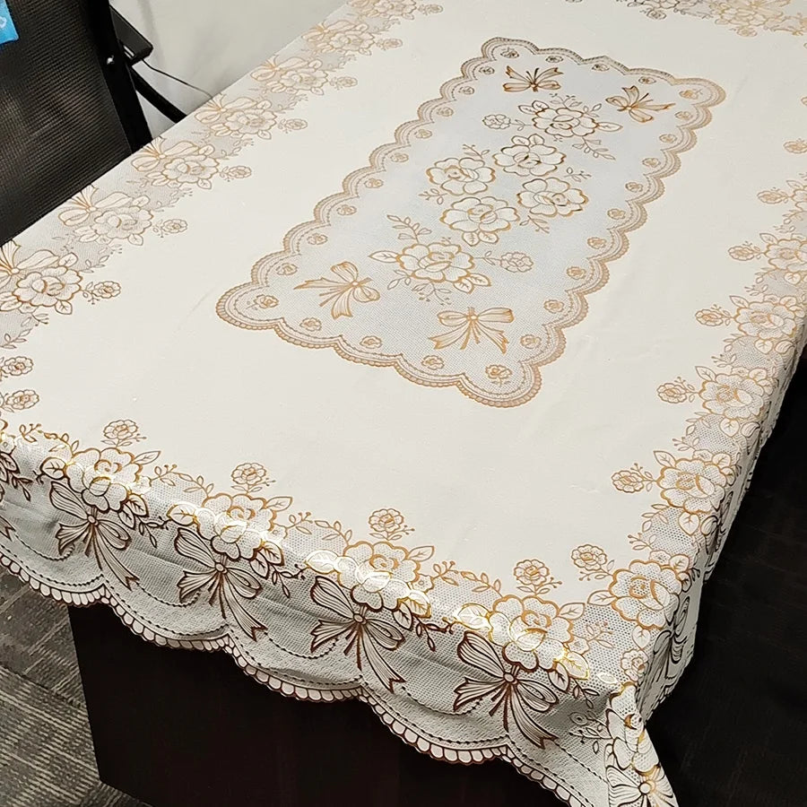 A rectangular dining table covered with a white cloth featuring gold floral embroidery and lace trim.