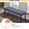 A gray stretch jacquard dining bench cover with unique straps shown on a wooden bench placed on a rug.