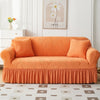 An orange jacquard elastic sofa cover with a ruffled skirt displayed in a bright room.