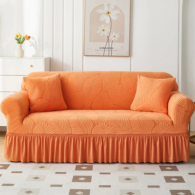 An orange jacquard elastic sofa cover with a ruffled skirt displayed in a bright room.