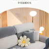 A modern gray sofa with white cushions and a yellow flower decoration is shown in a bright interior setting.