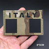 A hand holds a rectangular tactical patch featuring the word ITALY in camouflage pattern.