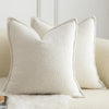 A close-up of a cream colored textured boucle throw pillow resting on a light sofa.