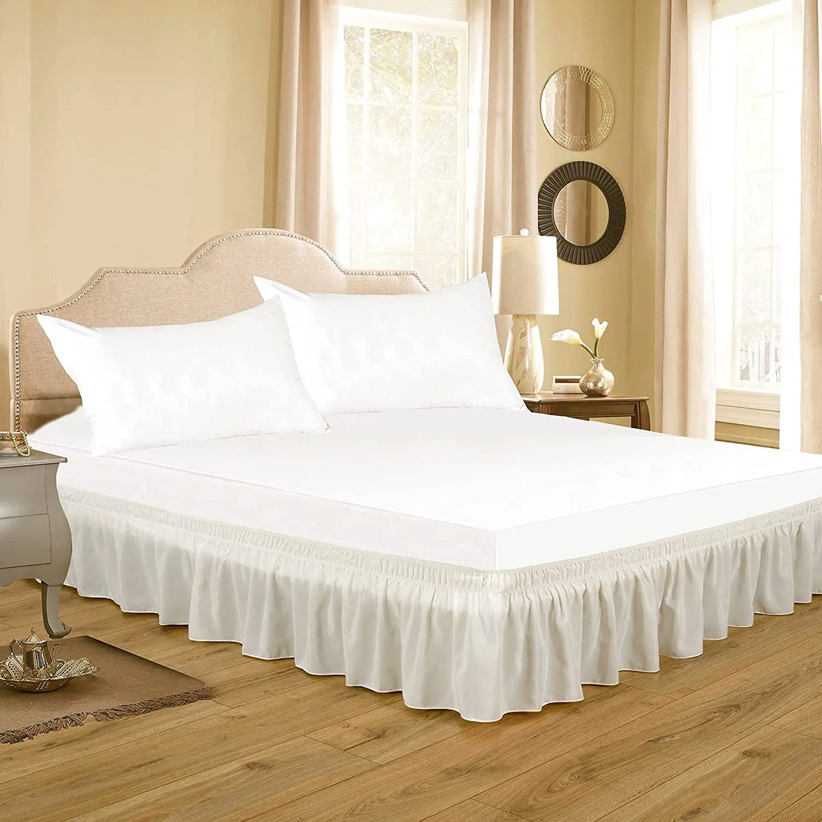 White bedding featuring a thick ruffle bed skirt and adjustable elastic belt on a wooden bed frame.