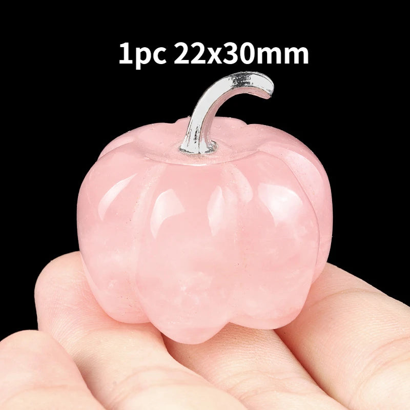 A pink natural stone pumpkin figurine with a silver stem is held in a person's hand.