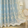 Light blue sheer floral curtains with lace trim draped over a white upholstered chair.