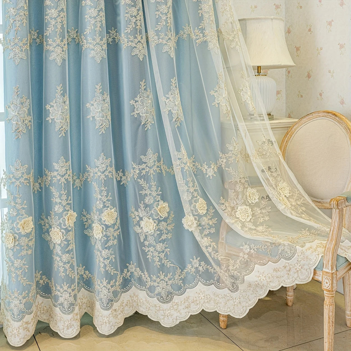 Light blue sheer floral curtains with lace trim draped over a white upholstered chair.