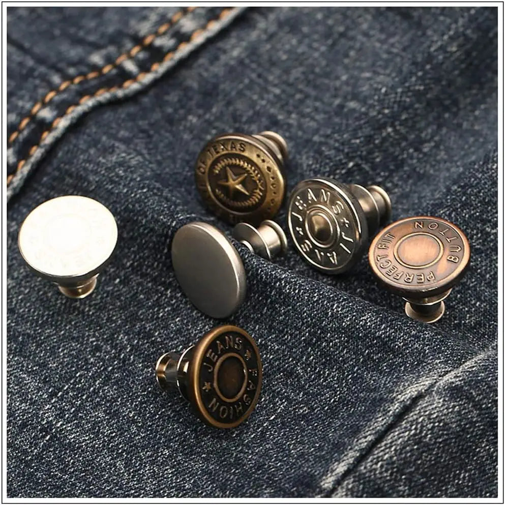 A collection of antique brass and silver adjustable button pins resting on a dark denim fabric.
