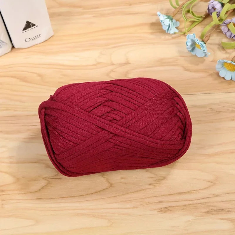 A ball of deep red flat thread yarn is lying on a light wooden surface.