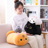 A woman is sitting on a couch with several soft cat plush toys, including a large yellow and black cat, a white cat, and a bl