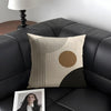 A beige cushion cover featuring minimalist geometric lines and a large circular brown shape on a dark gray sofa.