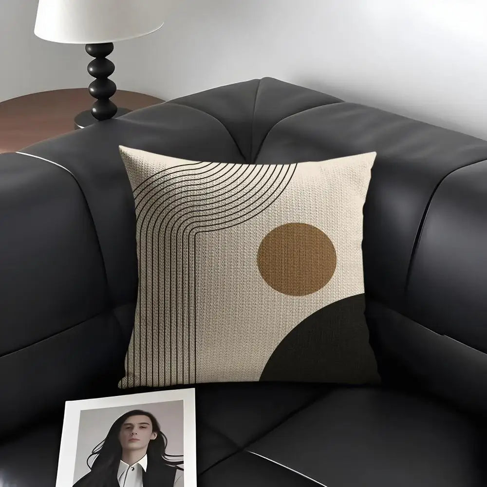 A beige cushion cover featuring minimalist geometric lines and a large circular brown shape on a dark gray sofa.