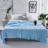 A light blue bamboo fiber cooling blanket is spread on a bed with white pillows and a framed art print.