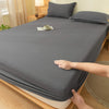 A hand is folding a gray brushed elastic fitted bed sheet set on a wooden bed.