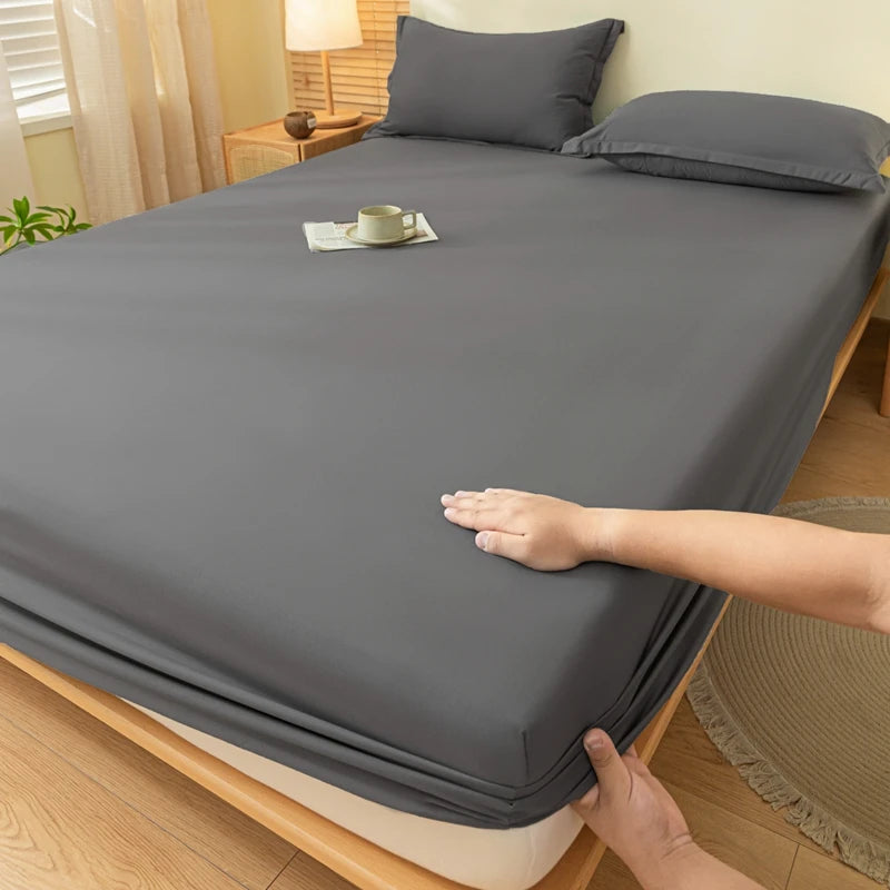 A hand is folding a gray brushed elastic fitted bed sheet set on a wooden bed.