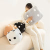 A woman is holding a gray plush dice cube cushion and several black and white polka dot cushions on a light-colored sofa.