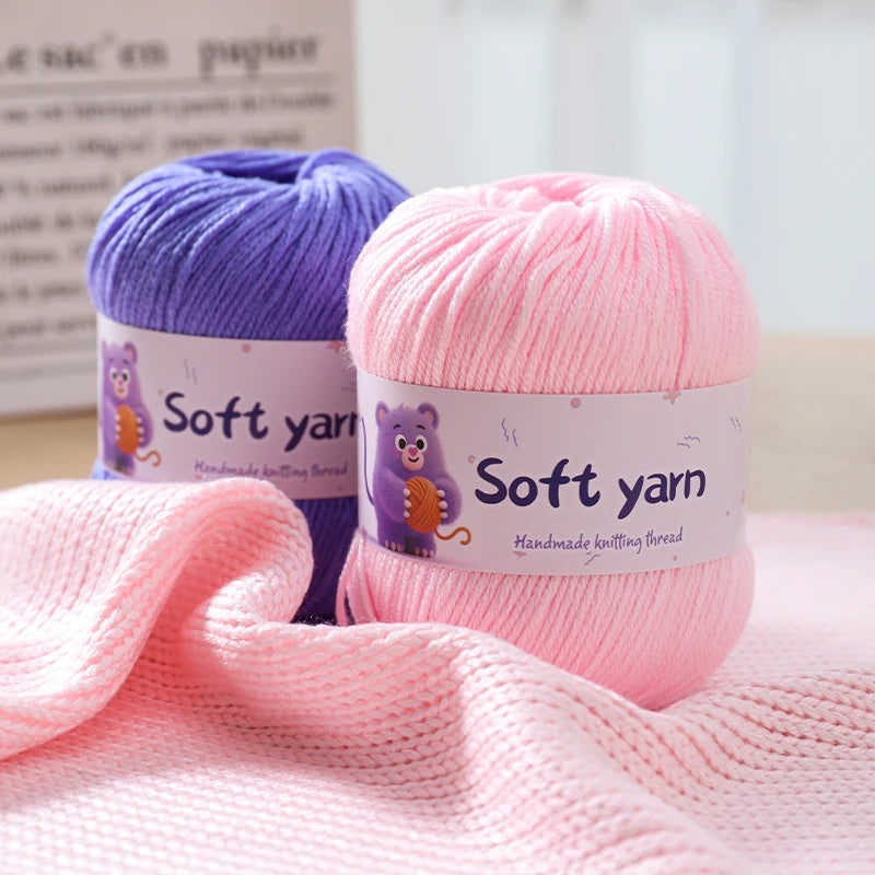 Two skeins of soft yarn, purple and pink, are displayed next to a pink knitted fabric.