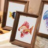 A wooden framed cross stitch kit featuring a colorful fish design on white fabric.