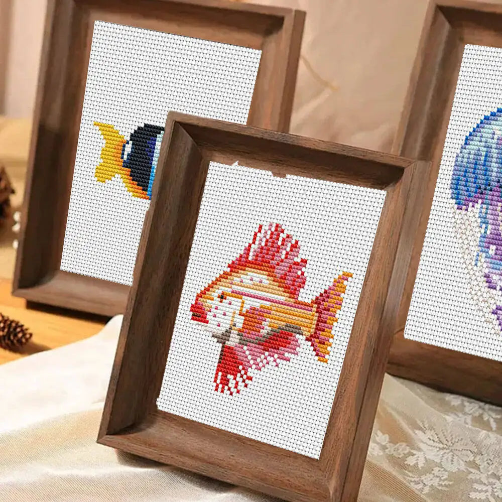 A wooden framed cross stitch kit featuring a colorful fish design on white fabric.
