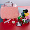 A pink portable sewing kit with a handle is shown next to various spools of thread and sewing tools on a red surface.