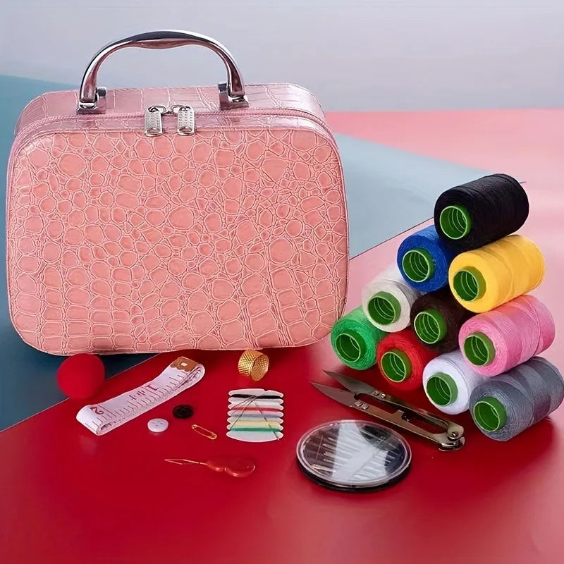 A pink portable sewing kit with a handle is shown next to various spools of thread and sewing tools on a red surface.
