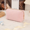 A pale pink, ribbed cosmetic storage pouch with gold hardware resting on a white textured surface.