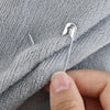 A hand is pinning a silver safety pin onto a gray towel fabric.