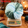 A ball of light blue and green chunky acrylic yarn resting on a digital scale for measuring knitting and crochet projects.