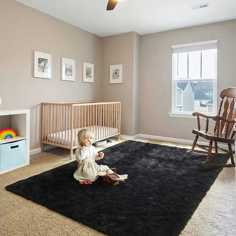 A modern black shag rug placed on a light carpet in a room with a wooden crib and window.