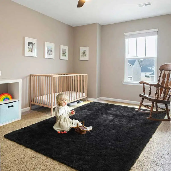 A modern black shag rug placed on a light carpet in a room with a wooden crib and window.