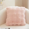 A square, light pink faux rabbit fur decorative throw pillow resting on a white sofa.