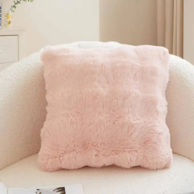 A square, light pink faux rabbit fur decorative throw pillow resting on a white sofa.