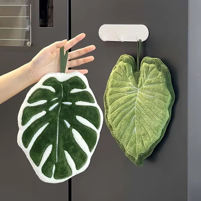 A hand is holding a green leaf-shaped absorbent microfiber towel against a dark gray background.