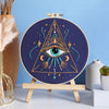 A dark blue embroidery featuring a triangle design with an eye motif and star patterns on a wooden easel.