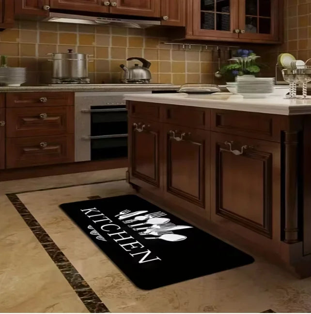 A black non-slip flannel area rug is placed on a light wood floor in a kitchen setting.