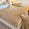 A beige jacquard weave fitted sheet bedding set on a white bed with matching pillows and a bedside lamp.