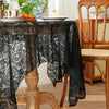 Black lace tablecloth draped over a wooden table with fruit and a dining chair in the background.